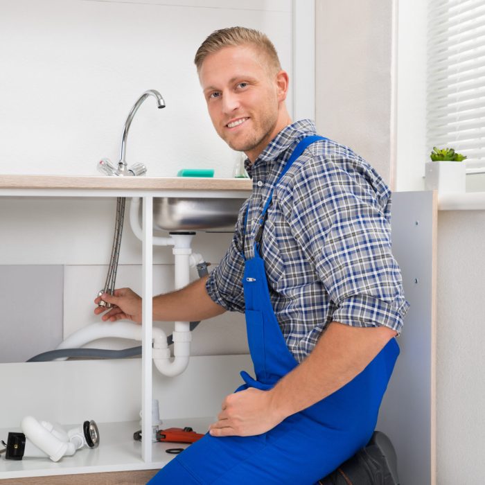 Happy Male Plumber Repairing Faucet In Kitchen Sink